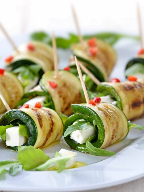 Zucchini-Röllchen mit Feta werden auf einem Teller mit etwas Rucola serviert.