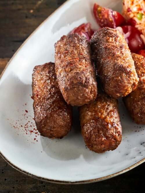 Cevapcici werden auf einer weißen Platte mit Djuvecreis serviert.