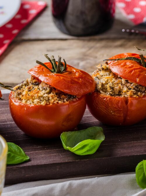 Faszerowane pomidory podawane są na drewnianej desce ze świeżymi ziołami.