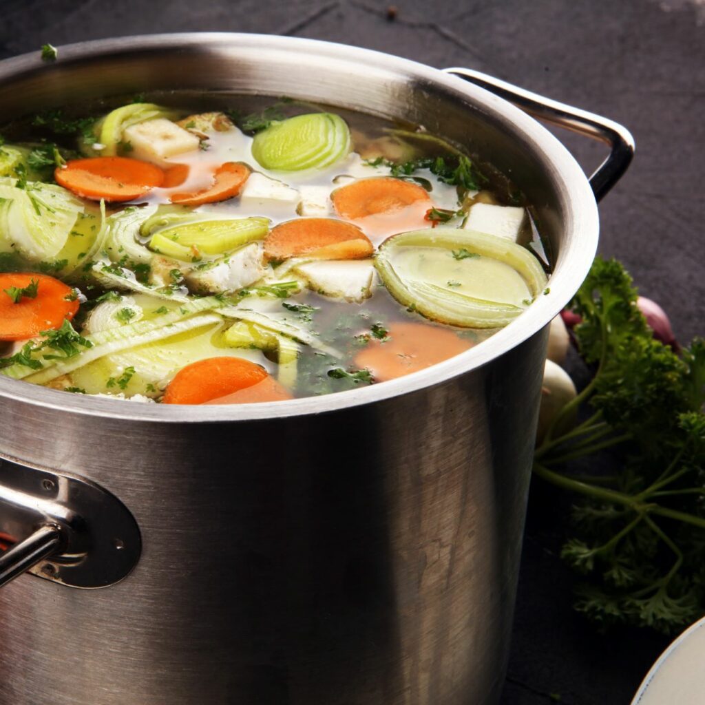 Rosół warzywny jest pokazywany w dużym rondlu przed odcedzeniem.