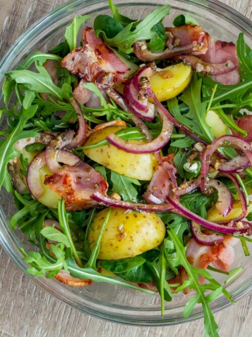 Kartoffel-Rucola-Salat wird von oben in einer Glasschüssel präsentiert.
