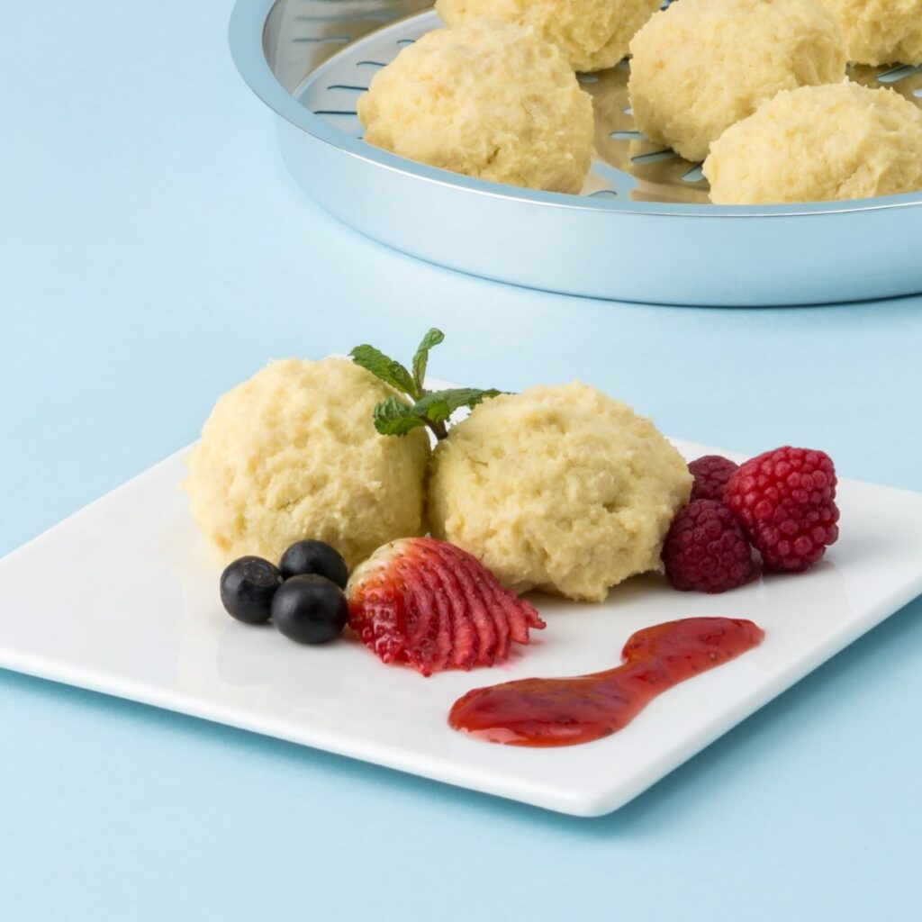 Quarkknödel aus der Heißluftfritteuse werden auf blauem Hintergrund mit frischen Beeren gezeigt.