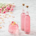 Syrop różany prezentowany jest w dwóch małych buteleczkach i szklance z kostkami lodu.