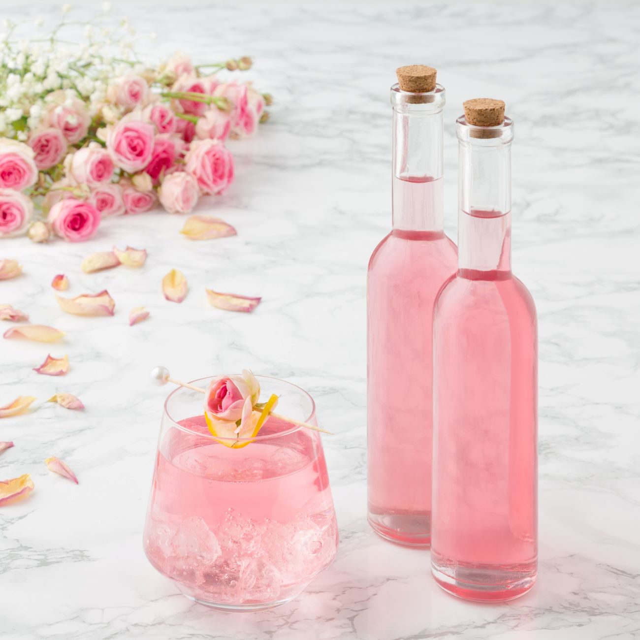Syrop różany prezentowany jest w dwóch małych buteleczkach i szklance z kostkami lodu.