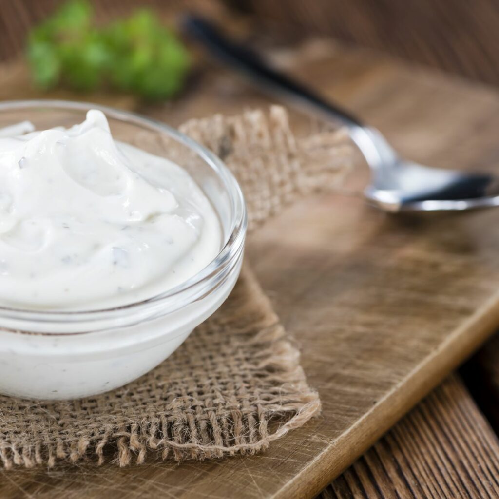 Vegane Sour Cream wird auf einem Holzbrett in einer kleinen Glasschale serviert.