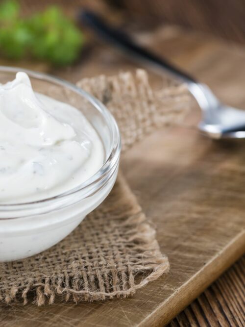 Vegane Sour Cream wird auf einem Holzbrett in einer kleinen Glasschale serviert.
