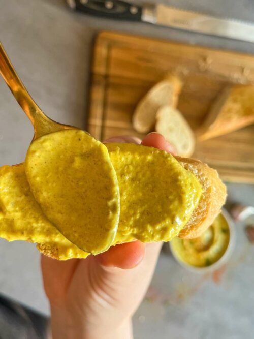 Curry-Dattel-Dip wird mit einem Löffel auf einem Stück Baguette verteilt.