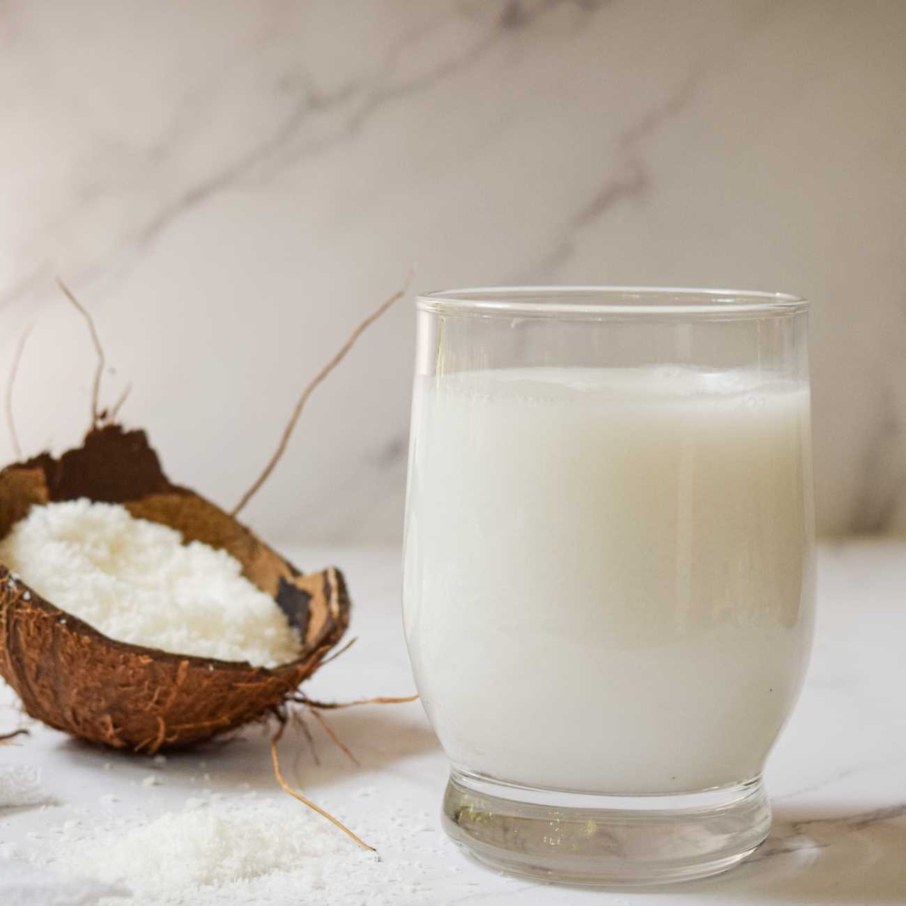 Mleko kokosowe jest pokazane z wiórkami kokosowymi i łupinami orzecha kokosowego.
