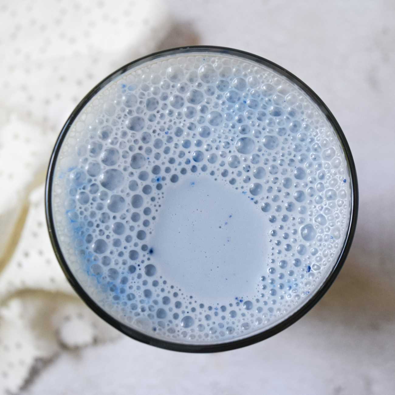 Blaue Mandelmilch wird von oben in einem Glas auf einem grauen Untergrund gezeigt.