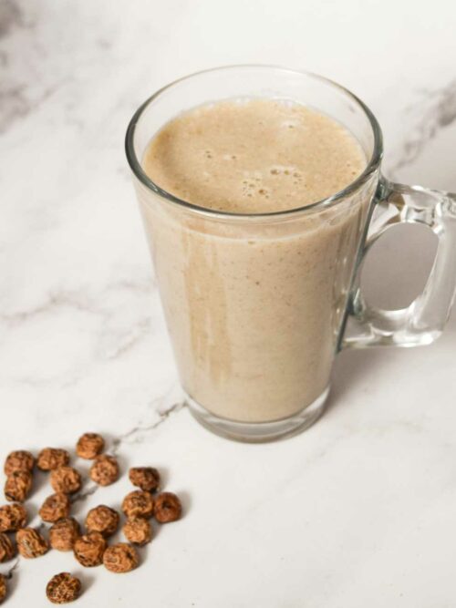 Horchata wir in einer gläsernen Tasse mit ein paar Erdmandeln vor einem Marmor-Hintergrund gezeigt.