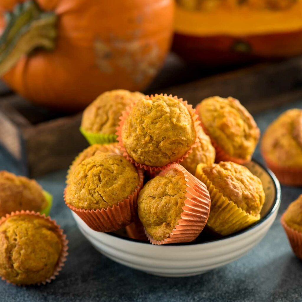 Muffinki dyniowe są ułożone w misce z dyniami w tle.