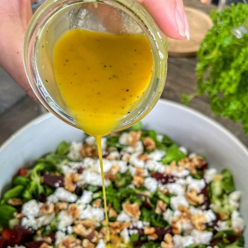 Honig-Senf-Dressing wird gezeigt, wie es gerade aus einem Glas über einen Salat geschüttet wird.