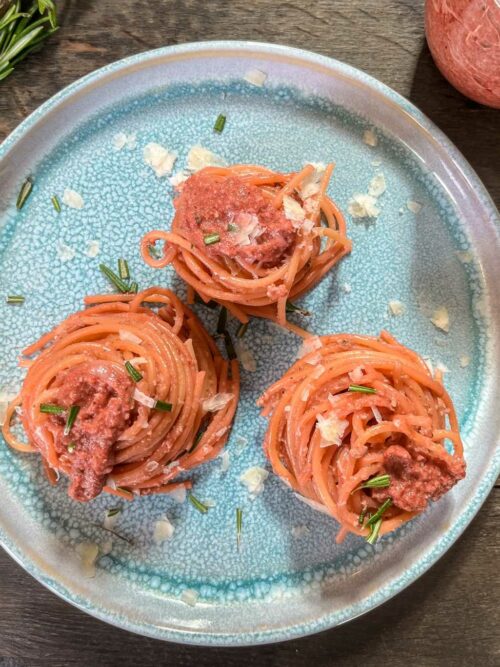Rote Bete Pesto mit Spaghetti wird auf einem blauen Teller mit Rosmarin und Parmesan serviert.