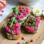 Rote Bete Hummus wird mit Rucola auf Baguette serviert.