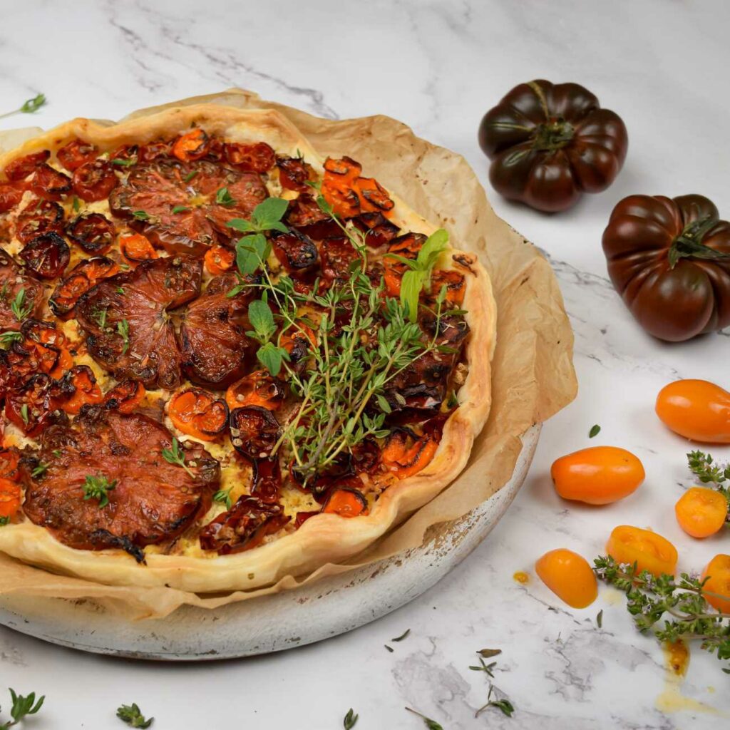 Tomaten Quiche wird mit Backpapier auf einem Brett gezeigt.