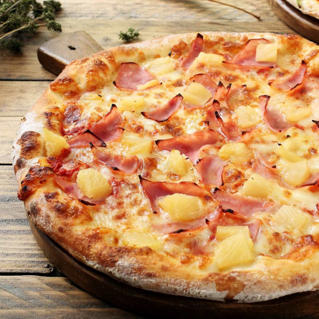 Pizza Hawaii wird auf einem runden Holzbrett serviert.