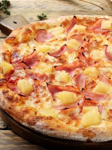 Pizza Hawaii wird auf einem runden Holzbrett serviert.