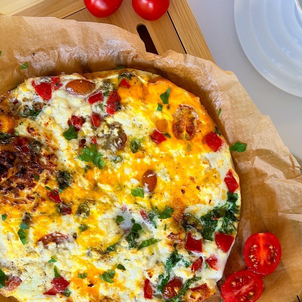 Frittata aus der Heißluftfritteuse wird mit Backpapier auf einem Holzbrett gezeigt.