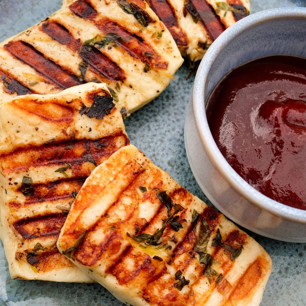 Halloumi grillen: Halloumi wird auf einem Teller mit roter Sauce gezeigt.