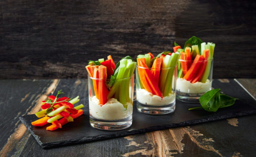 Zdrowe przekąski: paluszki warzywne są pokazane w szklance z dipem na dnie.
