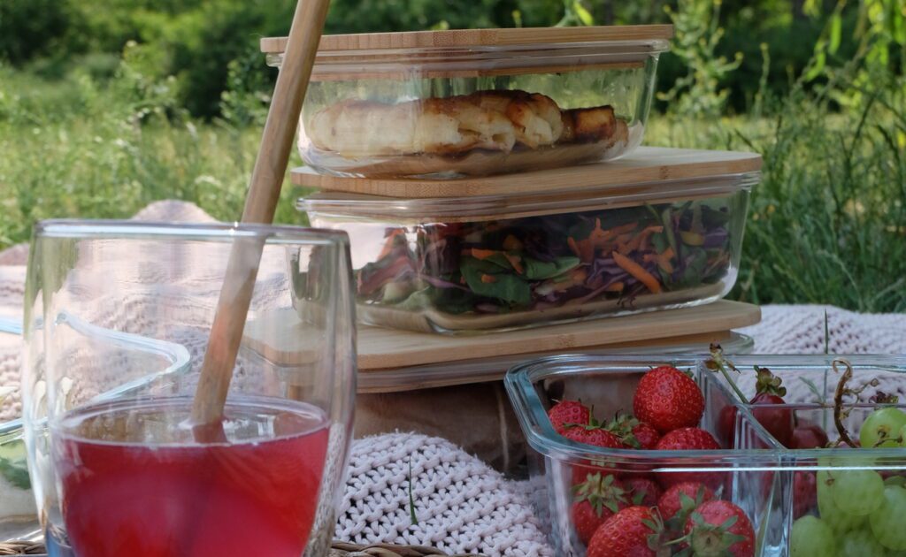 Zdrowe przekąski: praktyczne pudełka śniadaniowe firmy Klarstein są pokazane na kocu piknikowym.