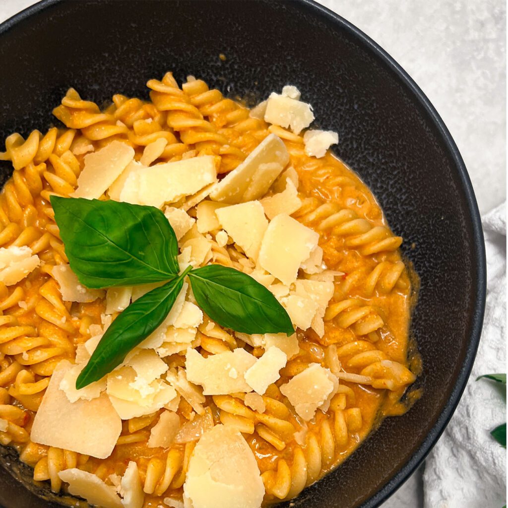 Kürbis Pasta wird in einer dunklen Schüssel mit Parmesan und Basilikum serviert.